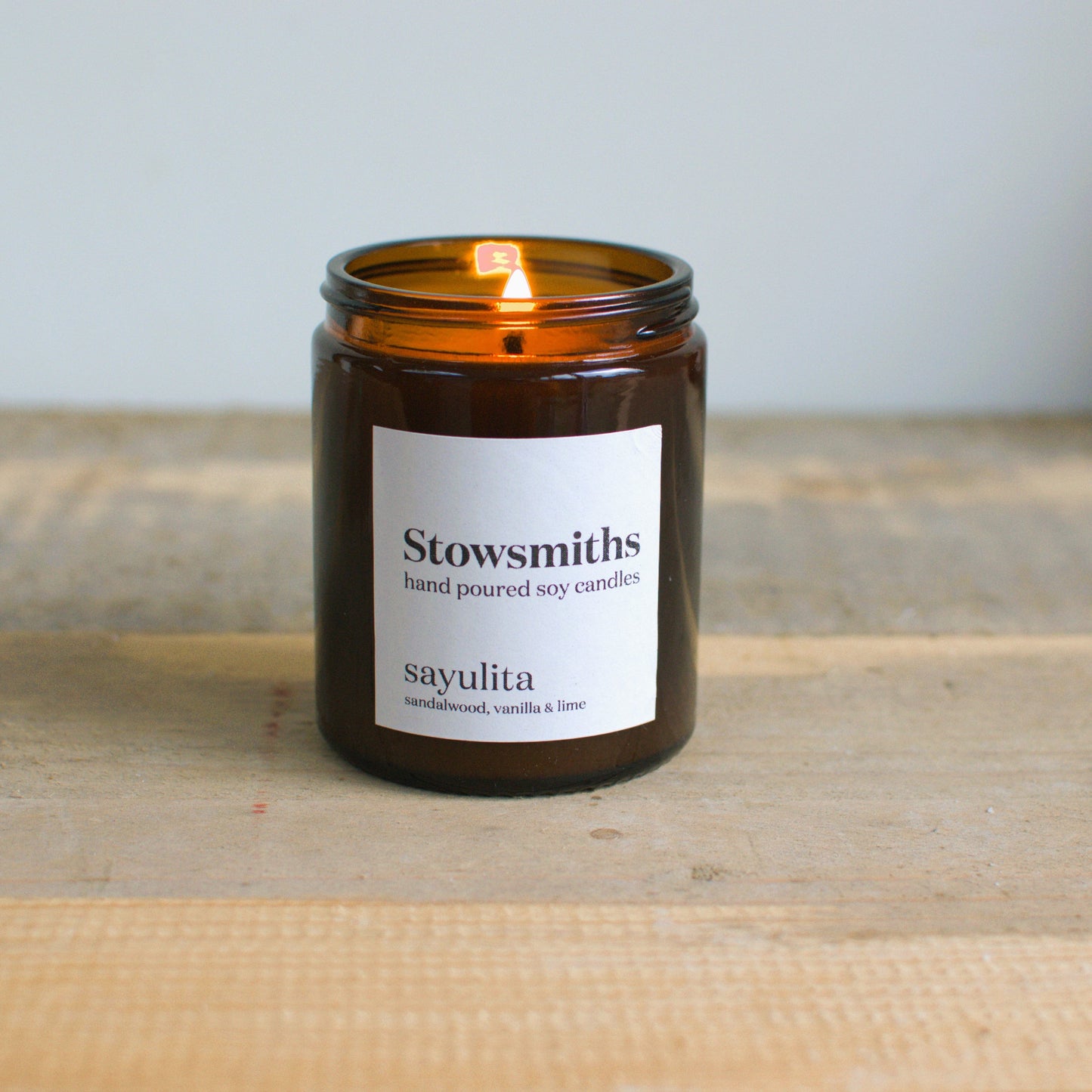 Coconut and lime scented hand poured candle lit and resting on a wooden surface. 