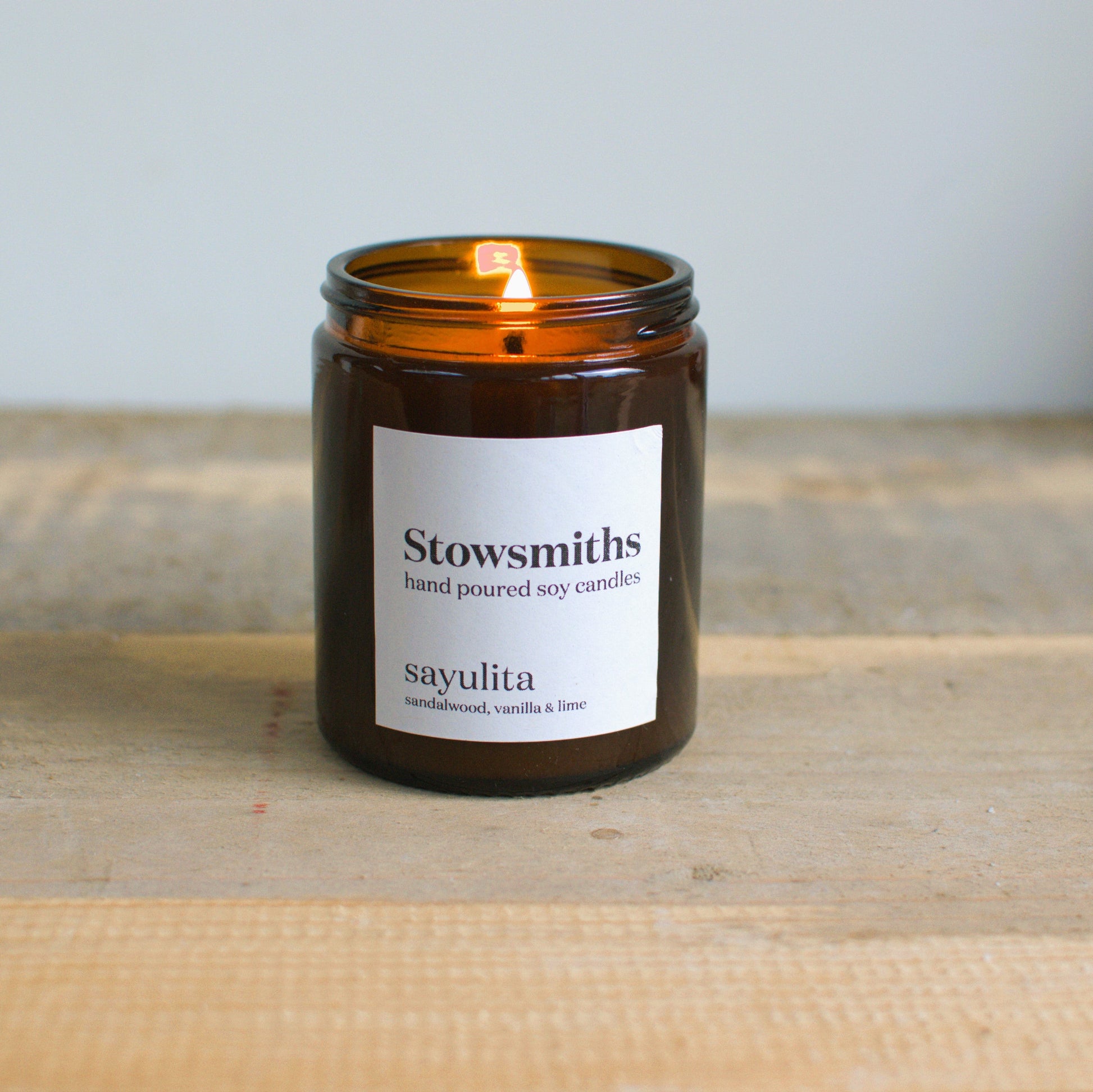 Coconut and lime scented hand poured candle lit and resting on a wooden surface. 